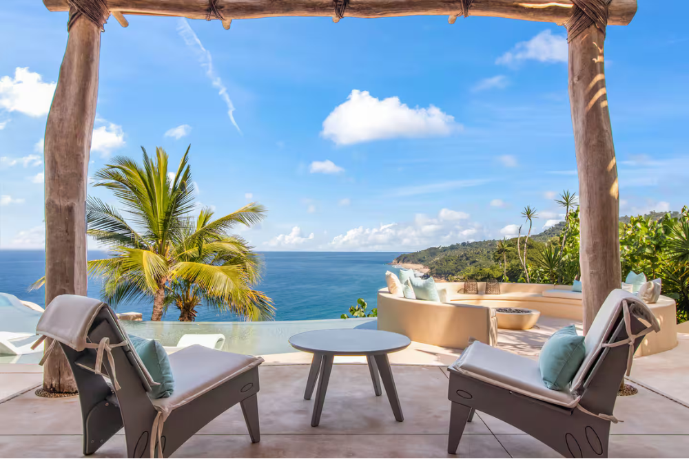 Row of sun loungers under white umbrellas facing an infinity pool and the ocean, offering a private sanctuary at a Sexual Wellness Retreat