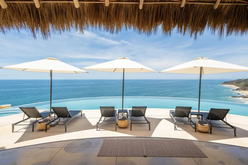 A luxury oceanfront villa at a Kama Sutra retreat at Fantasy Retreat, featuring an infinity pool with private lounge chairs and umbrellas overlooking the sea for a transformative couples experience.